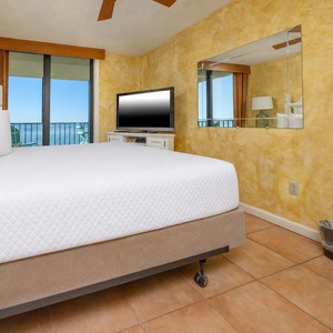 Bright, inviting master bedroom featuring a king bed, flat-screen TV, and a breathtaking view from the balcony