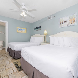 Two double beds with crisp white linens, a ceiling fan, and coastal decor create a relaxed atmosphere in this guest room