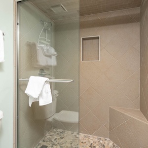 The sleek walk-in master bath shower features elegant tile work and a built-in shelf, complemented by fresh towels