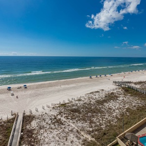 Beach view showcases white sand, colorful umbrellas, and the sparkling pool area framed by lush greenery