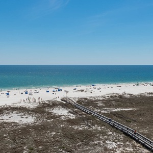 Expansive view of the beach with soft white sand, dotted with colorful umbrellas and a wooden walkway leading to the shore