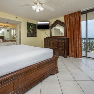 The elegantly furnished master bedroom features a king bed, a dresser, and the balcony door with views beyond