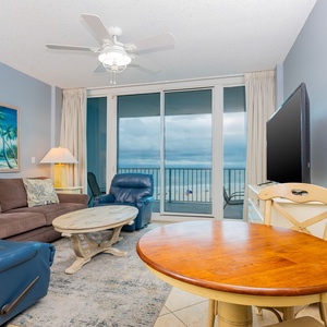 The living area features a cozy couch, a TV, and a stunning beachfront view through large sliding glass doors
