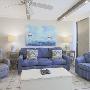 This living area features comfortable blue-striped seating, a TV on a white coffee table, and a vibrant nautical painting