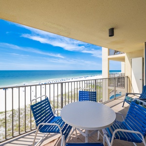 Patio table and blue lounge chairs, offering a serene view of the beach and sparkling water