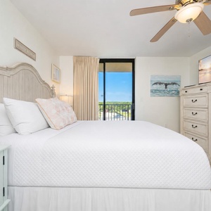 Master bedroom featuring a king bed with decorative pillows, a TV, and a balcony view overlooking the surrounding area