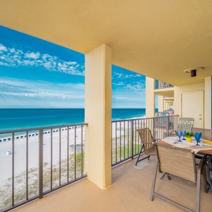 The balcony features a dining set with colorful tableware, offering a panoramic view of the beach and vibrant blue waters