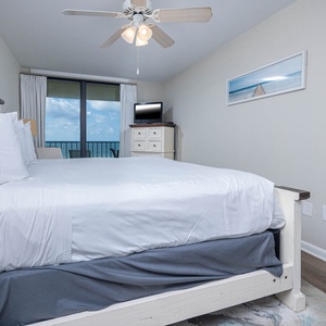 Cozy master bedroom featuring a plush king bed, a flat-screen TV, and a balcony with a captivating coastal view