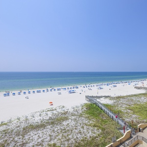 A panoramic view showcases the vibrant beach with blue umbrellas, white sand, and a clear sky, inviting relaxation and fun