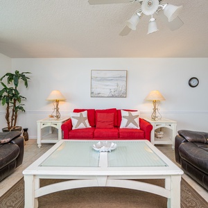 Red sofa with starfish pillows complements dark leather seating, creating a welcoming living area with coastal decor