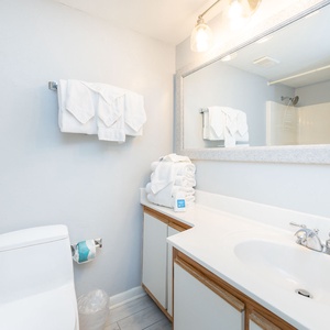 Bright and clean guest bathroom featuring a spacious vanity, neatly stacked towels, and a tub/shower combo