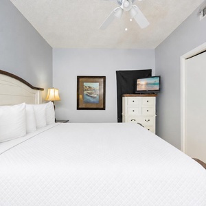 Cozy bedroom featuring a king bed with white linens, a framed nautical artwork, and a TV atop a white dresser