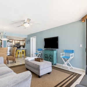 Living area featuring a comfortable gray sofa, stylish turquoise accents, TV, and a view of the dining space and kitchen