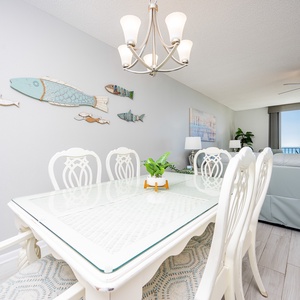 Bright dining area features a glass-top table with elegant white chairs, complemented by coastal decor