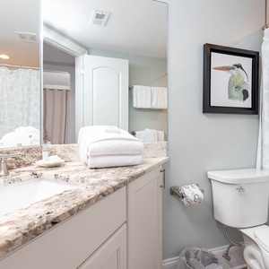 This bathroom features elegant granite countertops, soft white towels, and a charming coastal-themed shower curtain