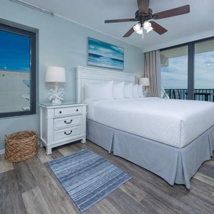 The master bedroom features a king-sized bed, coastal decor, and a stunning beachfront view through large windows