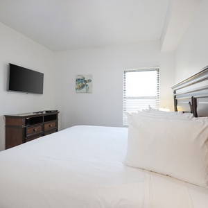 Guest bedroom featuring a large king bed, a flat-screen TV, and natural light streaming through the window