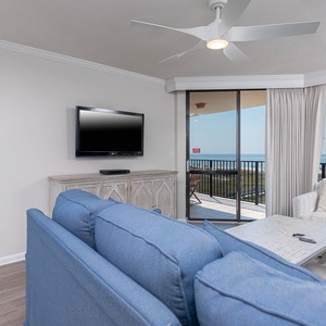 Cozy living area features a blue sofa with queen sleeper, a TV, and a balcony showcasing a beautiful beach front view