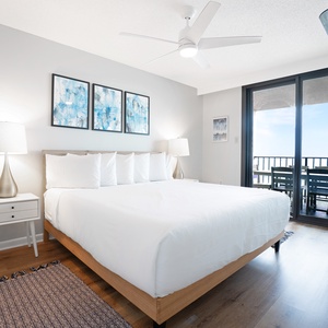 Brightly decorated master bedroom featuring a king bed, modern lamp, and the balcony view with outdoor seating
