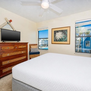 This bedroom features a cozy bed, a TV for entertainment, and windows offering a glimpse of the vibrant outdoor scenery