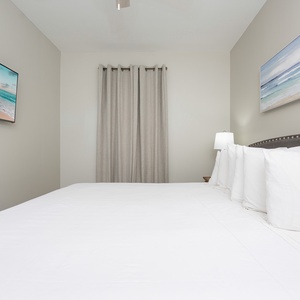 Brightly lit guest bedroom features a plush king bed with decorative pillows and a wall-mounted TV