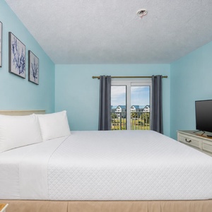 The master bedroom features a comfortable bed, a TV, and a lovely view from the balcony doors