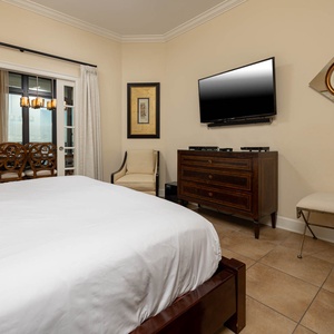 This cozy master bedroom features a king bed, sleek TV, elegant decor, and a view of the dining area through glass doors