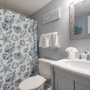 This bathroom features a stylish shell-patterned shower curtain, a sleek vanity, and fresh towels for a relaxing experience