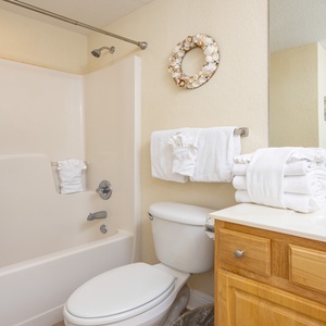 Bright and inviting guest bathroom featuring a tub/shower combo, fresh towels, and a coastal-inspired decorative wreath