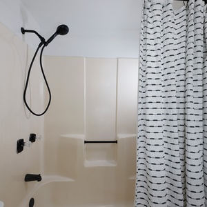 Relax in this modern guest bath featuring a sleek tub/shower with a stylish black and white curtain and plush white towels
