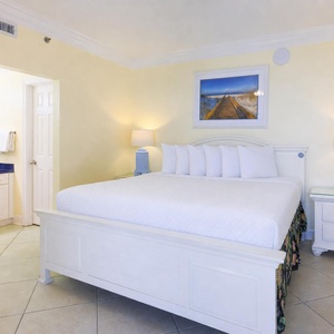 Master bedroom featuring a king bed, soft lighting, and a vibrant beach artwork, with an adjoining bathroom