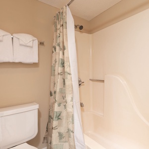 Master bath with a tub/shower combo with a patterned curtain and neatly arranged white towels above the toilet