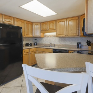 This kitchen features black appliances, wooden cabinetry, and a breakfast bar with white chairs for casual dining