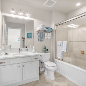 The guest bathroom features a bright, clean design with white cabinetry, a spacious vanity, and decorative coastal artwork