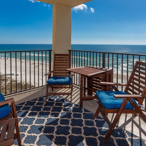 Relax on the balcony with comfortable seating and a table, enjoying the beautiful beachfront view and vibrant blue waters
