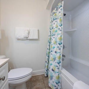 Guest bathroom featuring a tub/shower with colorful curtain and sleek vanity with ample space for toiletries