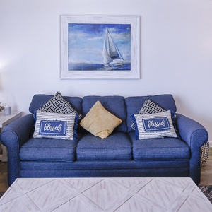 A cozy living area features a blue sofa adorned with decorative pillows, a stylish coffee table, and nautical-themed artwork