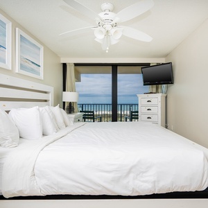 This bedroom features a plush white bed, a TV, and stunning beach front views through large sliding glass doors