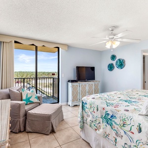 Brightly decorated master bedroom features a king bed with colorful bedding, a cozy seating area, and a balcony with a view
