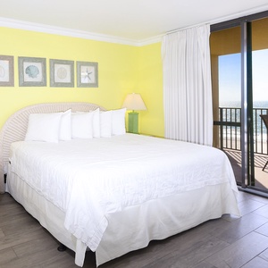 Cozy master bedroom featuring a king bed featuring bright yellow walls with a balcony offering a view of the beach