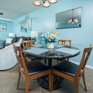 The dining area features a round granite table with four black chairs, complemented by blue walls and beach decor