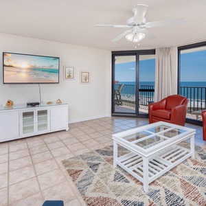 Bright living area features red leather chairs, a glass-top coffee table, and expansive views of the gulf from large windows