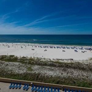 Balcony beach view with white sand, vibrant umbrellas, and gentle waves under a clear blue sky