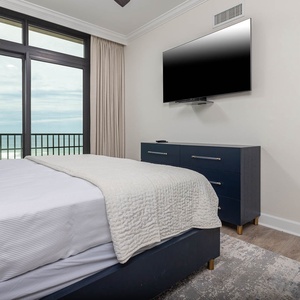 This bedroom features a large window with a beachfront view, a mounted TV, and stylish blue accents for a relaxing stay
