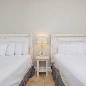 Cozy guest bedroom featuring two white double beds with plush pillows and a charming bedside lamp for a relaxing stay