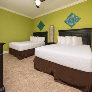 This guest bedroom features two cozy queen beds, a vibrant green accent wall, exciting décor, and a TV for entertainment