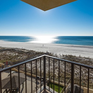 The view from the balcony showcases a serene beachfront with white sand and a sparkling sea under a clear blue sky