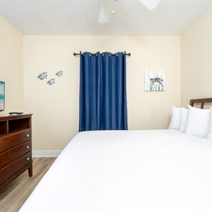 Guest bedroom featuring a large king bed, a TV, and vibrant blue curtains for a relaxing atmosphere
