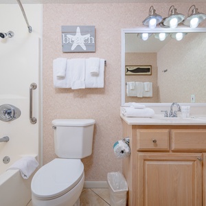The full bath features a tub/shower combo, light wood cabinetry, and beach decor for a refreshing retreat