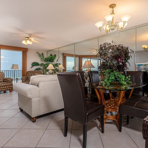 The inviting living area features comfortable seating, a dining table, and large windows offering a glimpse of the beach